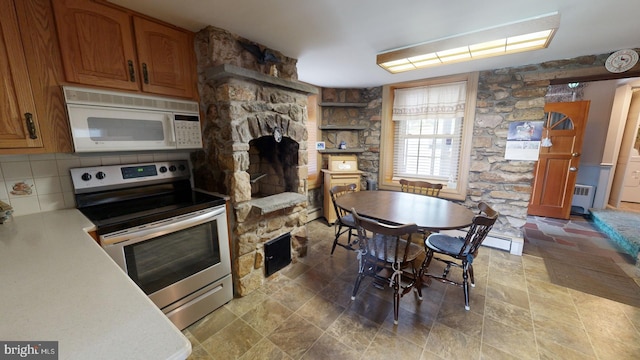 kitchen with backsplash, a stone fireplace, radiator heating unit, light tile patterned floors, and stainless steel electric range oven