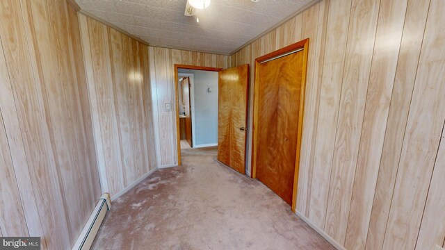 hall with carpet, wood walls, and a baseboard radiator