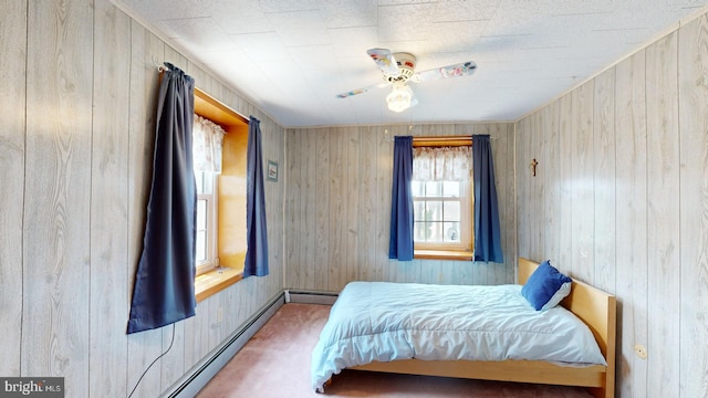 carpeted bedroom featuring ceiling fan, wood walls, and a baseboard heating unit