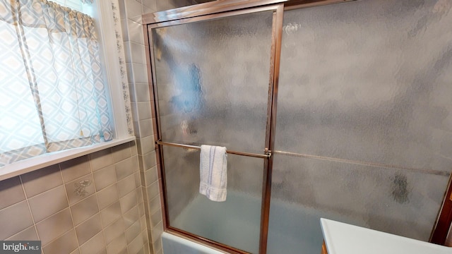 bathroom featuring combined bath / shower with glass door and tile walls