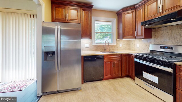 kitchen with appliances with stainless steel finishes, light hardwood / wood-style flooring, tasteful backsplash, sink, and light stone countertops