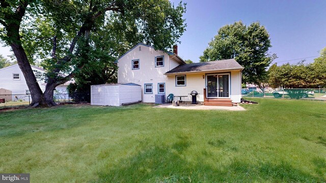 rear view of property featuring a lawn, a storage shed, and cooling unit