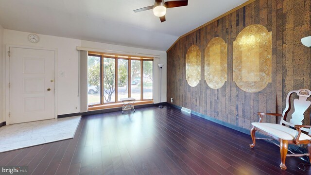 interior space with wood walls, ceiling fan, dark wood-type flooring, and vaulted ceiling