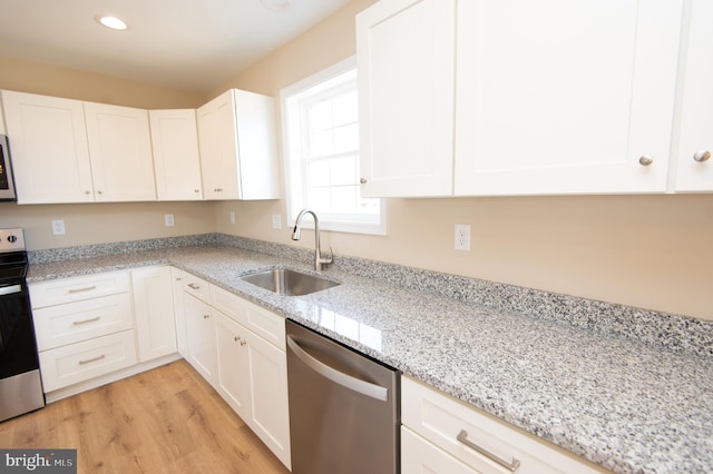 kitchen with appliances with stainless steel finishes, light wood-type flooring, light stone counters, sink, and white cabinetry