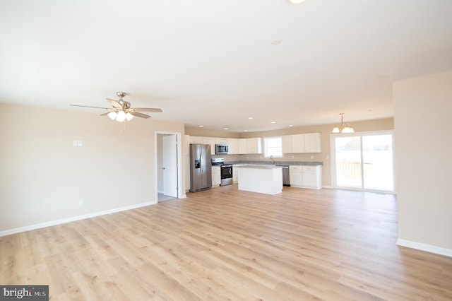 unfurnished living room featuring ceiling fan with notable chandelier and light hardwood / wood-style floors