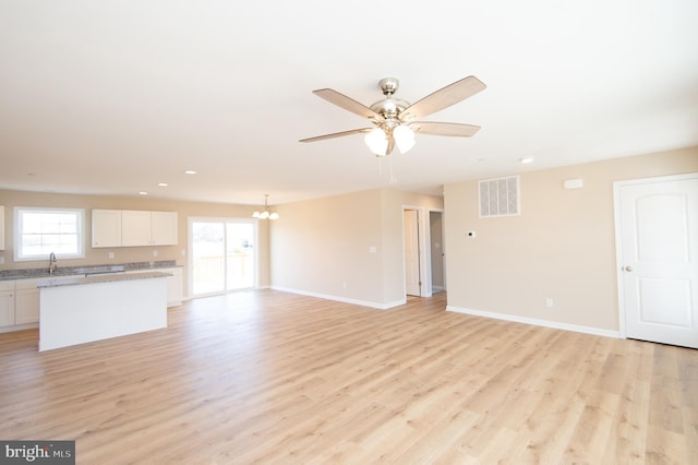 unfurnished living room featuring ceiling fan with notable chandelier, light hardwood / wood-style floors, and a healthy amount of sunlight