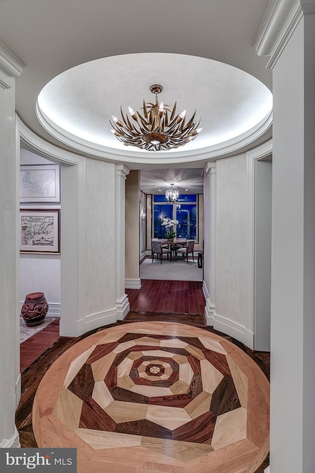 hallway featuring a notable chandelier, baseboards, parquet floors, a tray ceiling, and ornate columns