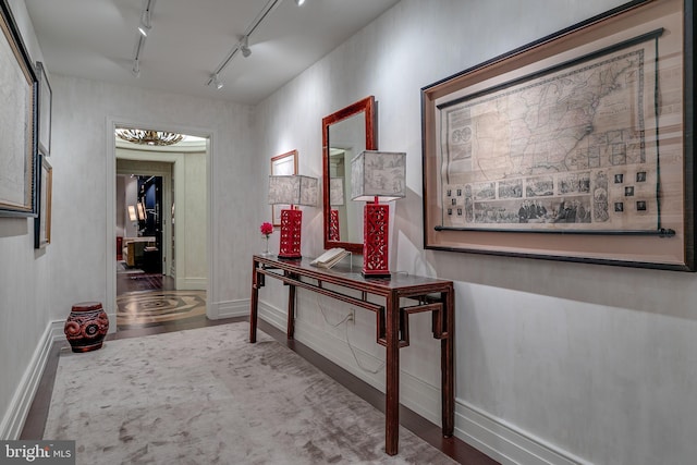 hallway featuring baseboards, wood finished floors, and track lighting