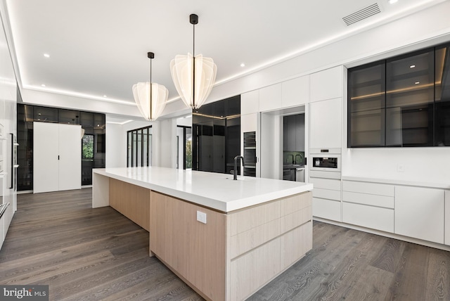 kitchen with a spacious island, white cabinets, decorative light fixtures, dark wood-type flooring, and light brown cabinetry