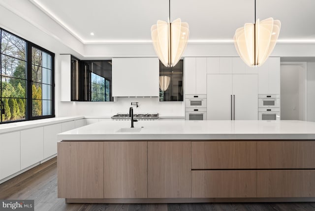 kitchen featuring white cabinets, white double oven, an island with sink, and pendant lighting