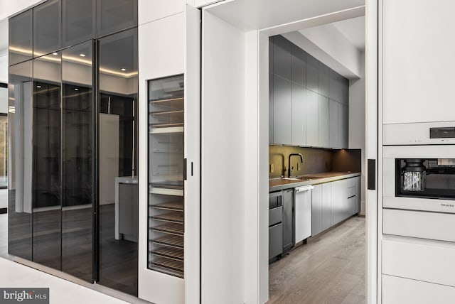 kitchen featuring stainless steel dishwasher, sink, oven, and light hardwood / wood-style flooring