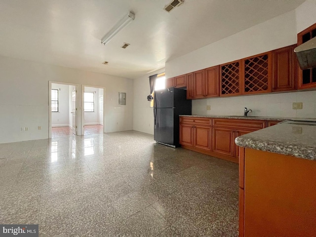 kitchen with backsplash, range hood, black fridge, and a wealth of natural light