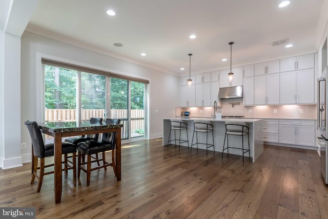 kitchen with a center island with sink, visible vents, decorative light fixtures, light countertops, and white cabinetry