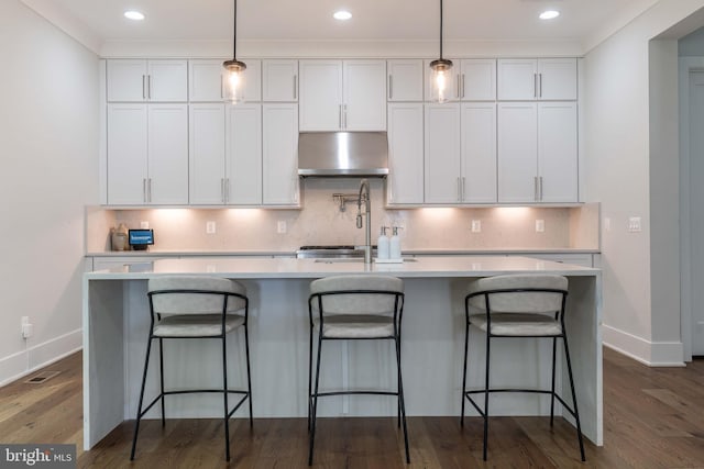 kitchen featuring under cabinet range hood, a center island with sink, white cabinetry, and light countertops