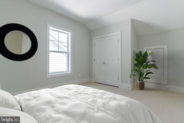 bedroom with light carpet, a closet, lofted ceiling, and baseboards