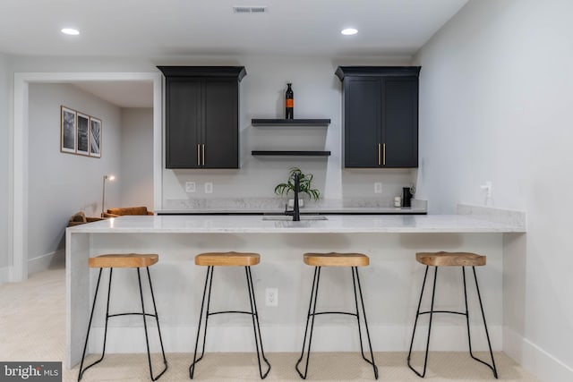 kitchen with visible vents, light stone countertops, dark cabinets, a peninsula, and a kitchen breakfast bar