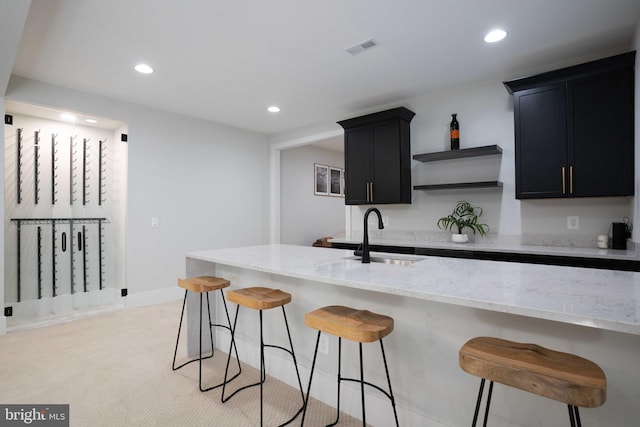 kitchen featuring light stone counters, recessed lighting, visible vents, a sink, and dark cabinets