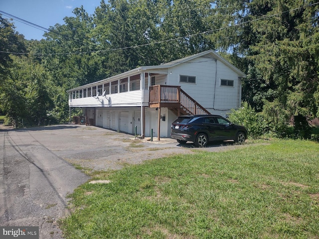 view of side of property featuring a wooden deck, a garage, a lawn, and a sunroom