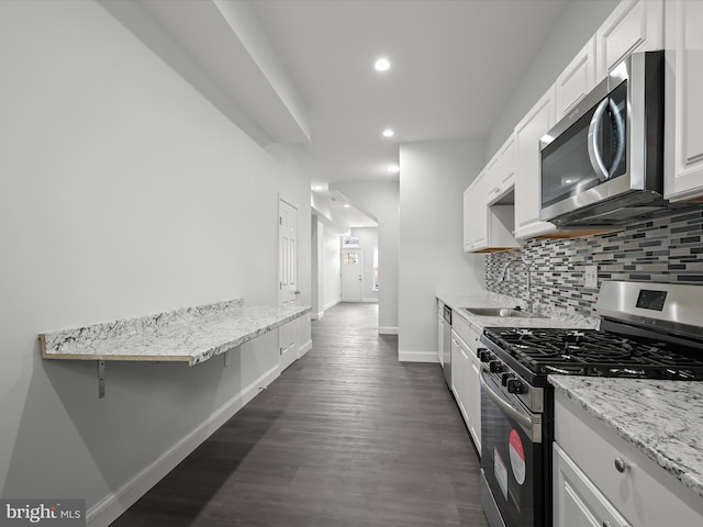 kitchen with stainless steel appliances, a sink, baseboards, white cabinets, and tasteful backsplash