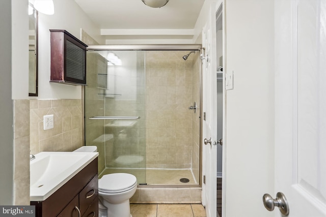 bathroom featuring tile patterned flooring, tile walls, vanity, toilet, and walk in shower