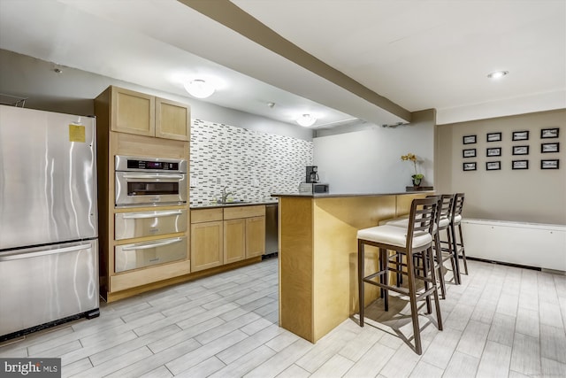 kitchen featuring sink, appliances with stainless steel finishes, a kitchen bar, decorative backsplash, and kitchen peninsula