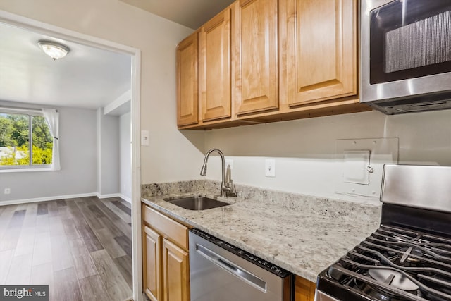 kitchen featuring stainless steel appliances, hardwood / wood-style flooring, sink, and light stone counters