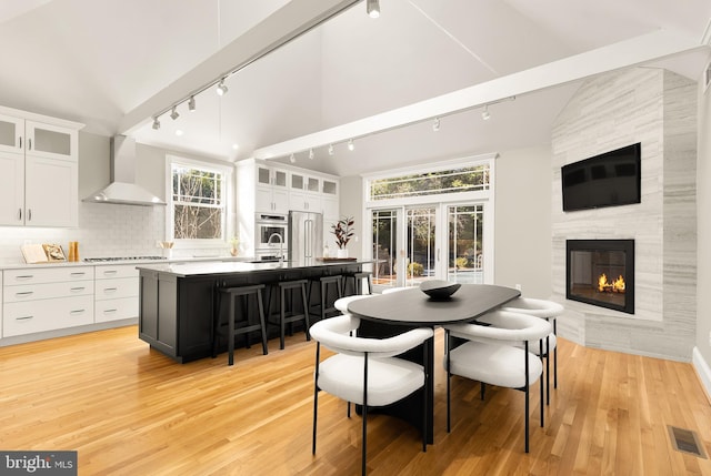 dining space featuring light wood-style floors, a fireplace, visible vents, and vaulted ceiling