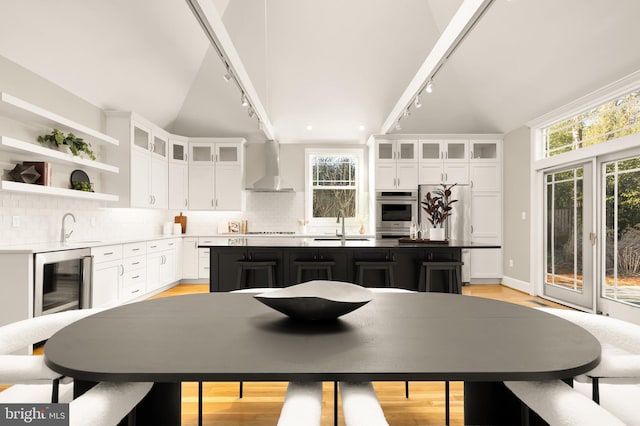 kitchen with a sink, white cabinets, wall chimney range hood, tasteful backsplash, and a center island with sink