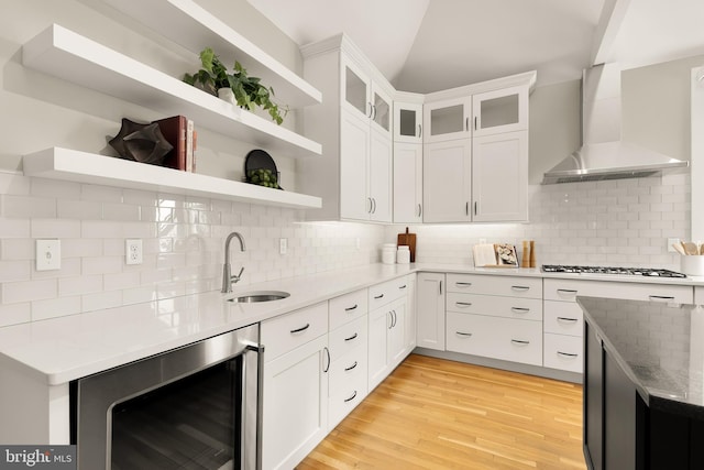 kitchen featuring beverage cooler, wall chimney exhaust hood, gas cooktop, open shelves, and a sink