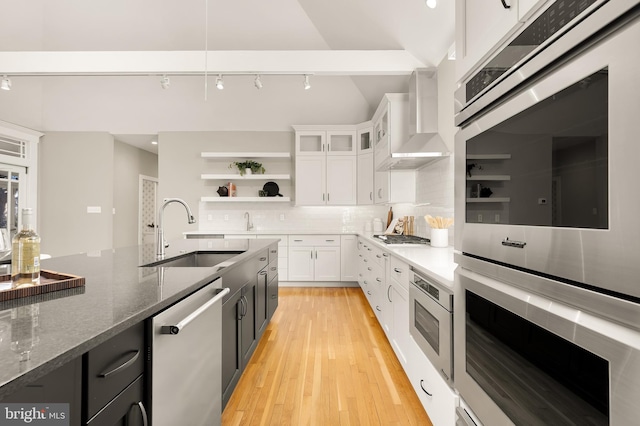 kitchen featuring open shelves, stainless steel appliances, backsplash, a sink, and wall chimney exhaust hood