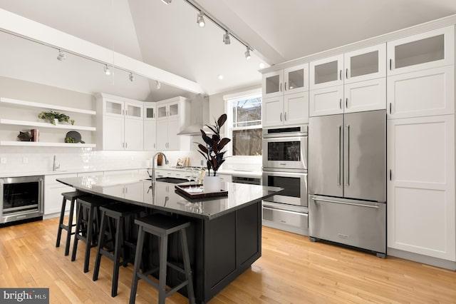 kitchen featuring stainless steel appliances, wine cooler, light wood-style floors, and wall chimney range hood