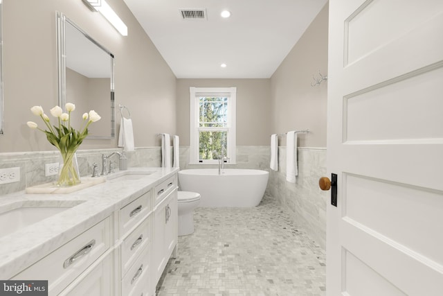 full bath with double vanity, visible vents, a wainscoted wall, a freestanding bath, and a sink