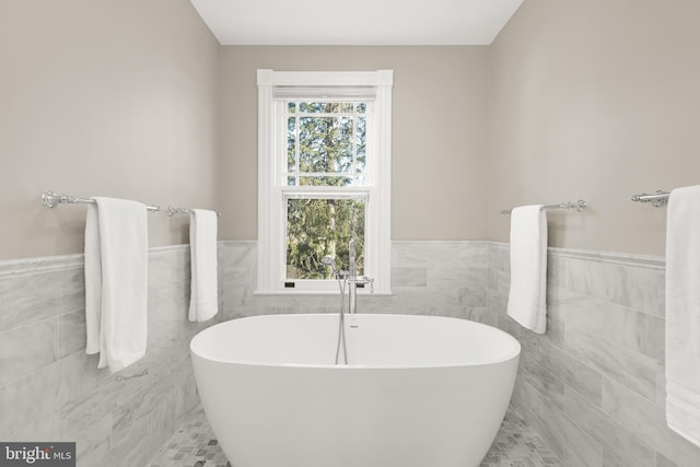 bathroom featuring a freestanding tub, a wainscoted wall, and tile walls