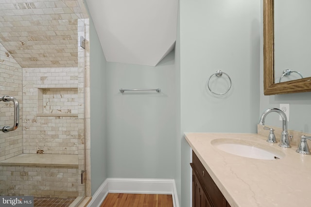 full bathroom with a stall shower, baseboards, lofted ceiling, wood finished floors, and vanity