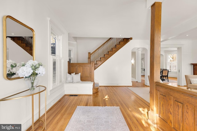 entrance foyer with arched walkways, wood finished floors, visible vents, baseboards, and stairway