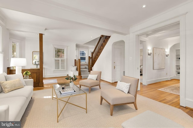 living room featuring arched walkways, ornamental molding, wood finished floors, beamed ceiling, and stairs