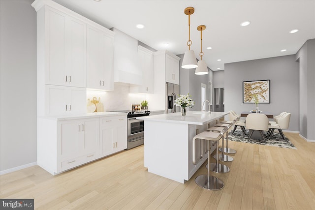 kitchen with premium range hood, stainless steel appliances, white cabinetry, hanging light fixtures, and an island with sink