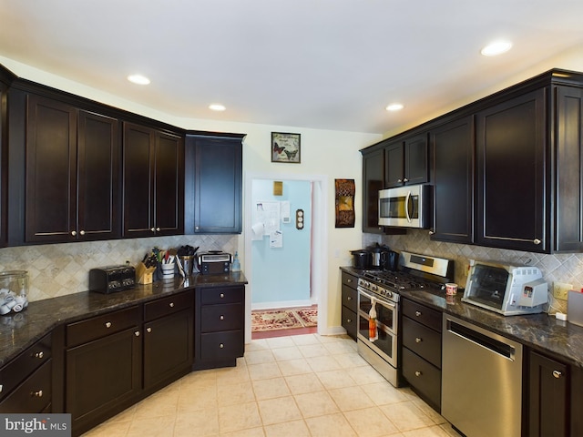 kitchen with light tile patterned floors, tasteful backsplash, stainless steel appliances, and dark stone counters