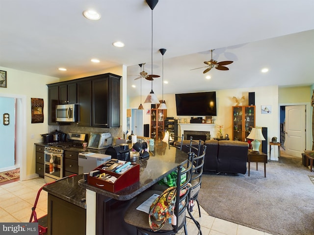 kitchen with a breakfast bar, a fireplace, decorative backsplash, appliances with stainless steel finishes, and ceiling fan