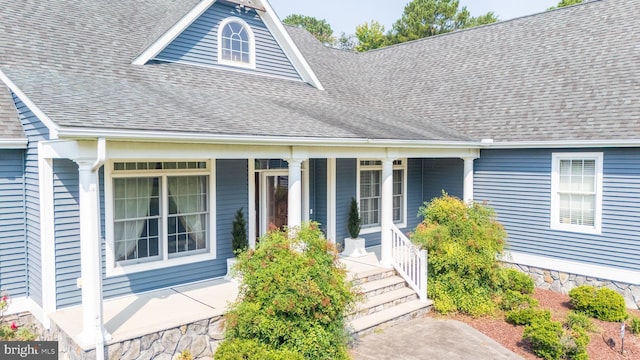 view of exterior entry featuring covered porch and a shingled roof