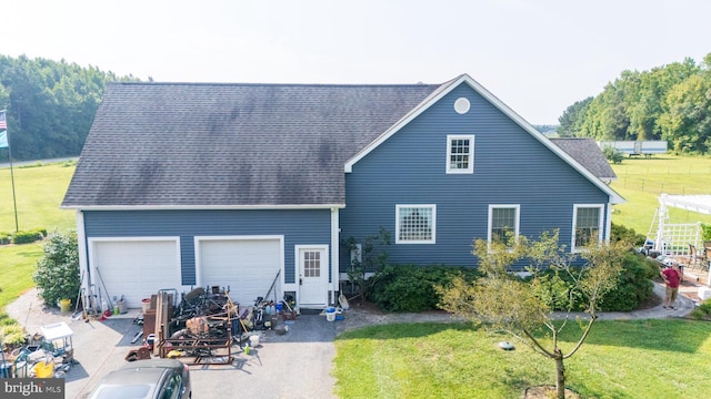 back of house with roof with shingles, a lawn, and an attached garage