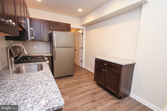 kitchen with dark brown cabinets, tasteful backsplash, light hardwood / wood-style floors, and stainless steel fridge