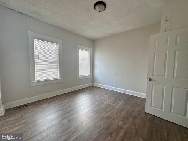 unfurnished room featuring dark wood-type flooring and a textured ceiling