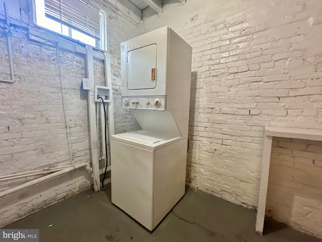 laundry area with brick wall and stacked washer / drying machine