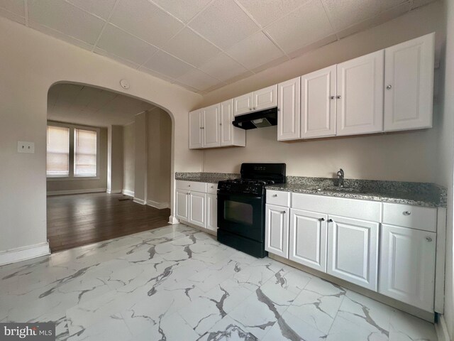 kitchen featuring black range, dark stone countertops, white cabinetry, a drop ceiling, and light tile patterned floors