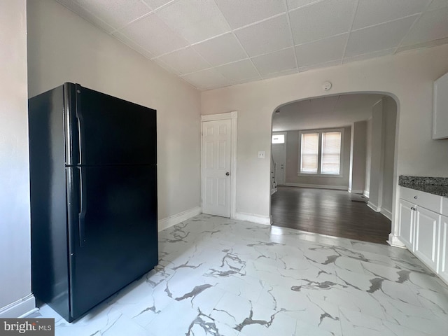 kitchen with a paneled ceiling, white cabinets, black fridge, and light hardwood / wood-style floors