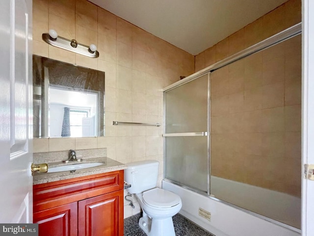 full bathroom with toilet, tile patterned flooring, enclosed tub / shower combo, tile walls, and vanity