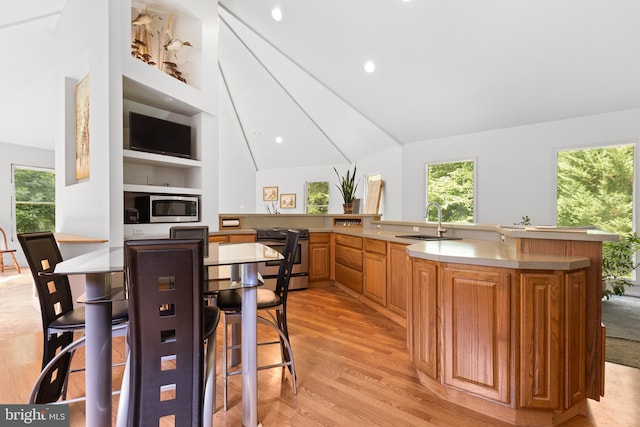 kitchen with a breakfast bar, sink, kitchen peninsula, stainless steel appliances, and light hardwood / wood-style flooring