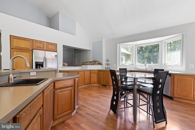 kitchen featuring high vaulted ceiling, stainless steel fridge, light hardwood / wood-style floors, and sink