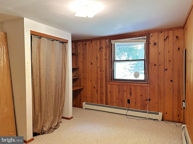 unfurnished bedroom featuring a baseboard heating unit, carpet, wooden walls, and a closet